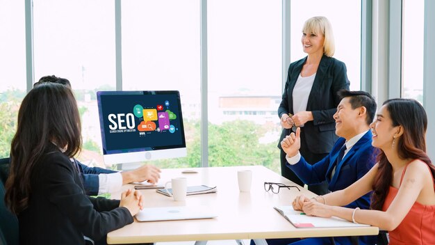 How Outsourced Local SEO Can Help Businesses Rank Higher 2 Business team in a meeting room discussing SEO strategies, with a presentation on a monitor and a woman leading the session.