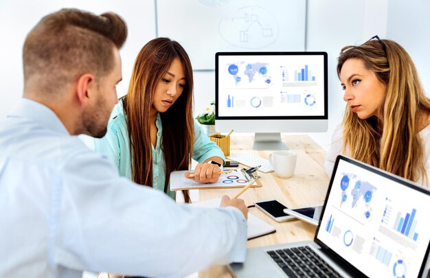How Outsourced Local SEO Can Help Businesses Rank Higher 3 Three coworkers analyzing data charts on laptops and monitors in a modern office during a digital marketing strategy meeting.