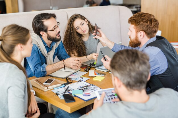 How Marketing Agencies Transform Ideas Into Results 2 Group of young professionals collaborating at a table with laptops, smartphones, color swatches, and printed charts during a creative meeting.